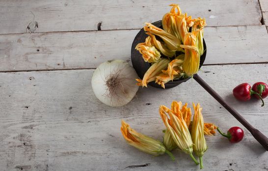 Fresh courgette flowers, chili peppers and onion on white table