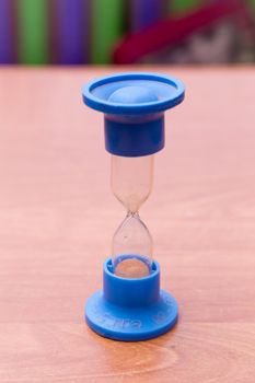 An antique hourglass on a blue leg stands upright on the table. The device counts the time and measures it very accurately. A device for measuring the time interval.