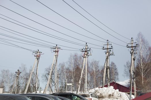 Electricity concept, concrete pillars with high voltage wires. Against the background of the blue sky, trees and snowdrifts. Power line close to high voltage transformer station.