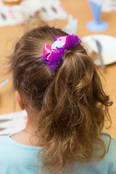 Close-up of a girl's hairstyle with a ponytail tied with a red bow. Hair styling is done with hairpins and an elastic band. Only the back of the head with a haircut.