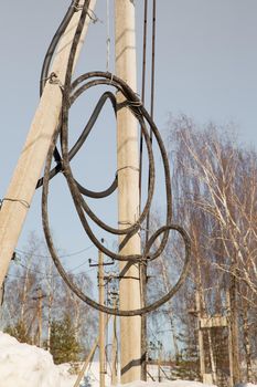 Electricity concept, concrete pole with high voltage cable coiled into a coil. Close-up against the blue sky. Power line close to high voltage transformer station.