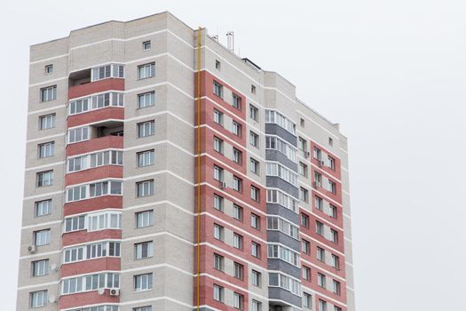 High-rise residential building with red brick balconies. Against the background of the gray sky. Modern new buildings, building facades. Real estate and urban architecture concept.