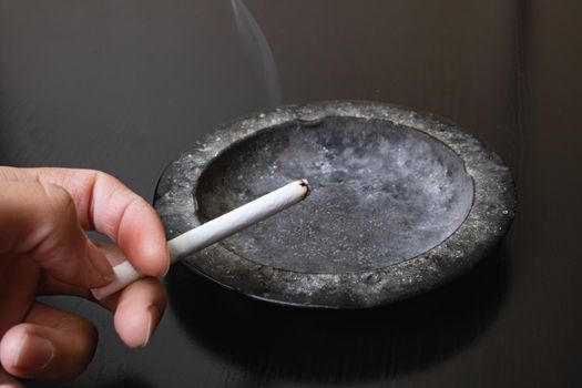 A lit cigarette in hand and an ashtray closeup
