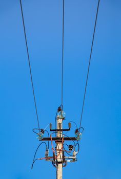 Electricity concept, top of a concrete pillar with high voltage wires. Close-up against the blue sky. Power line close to high voltage transformer station.