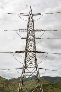 Image of high voltage electricity pylon and transmission power line with sky and mountain background.
