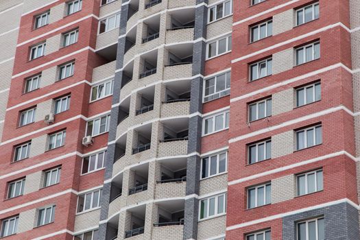 Windows and balconies of a high-rise building made of red and white bricks. Against the background of the gray sky. Modern new buildings, building facades. Real estate and urban architecture concept.