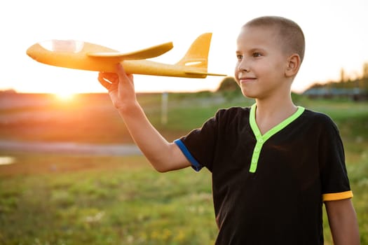 Boy throws a toy airplane in the summer at sunset. A child plays with a toy airplane, dreams of a trip. Son plays by plane in the field at sunset. Have fun and enjoy life