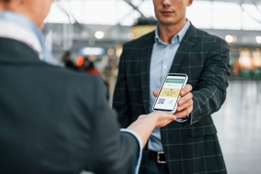 Holding and showing vaccination certificate. Young businessman in formal clothes is in the airport at daytime.