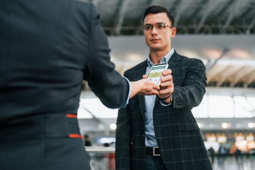 Holding and showing vaccination certificate. Young businessman in formal clothes is in the airport at daytime.