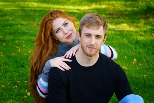 Cheerful young couple guy and red-haired girl of Caucasian ethnicity, are having fun together in the park on green grass on a sunny summer day in casual clothes