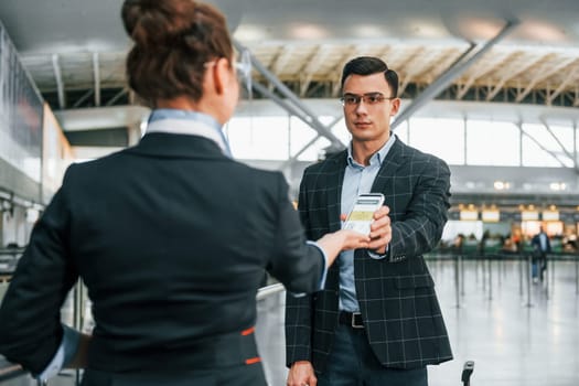 Holding and showing vaccination certificate. Young businessman in formal clothes is in the airport at daytime.