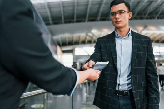 Holding and showing vaccination certificate. Young businessman in formal clothes is in the airport at daytime.