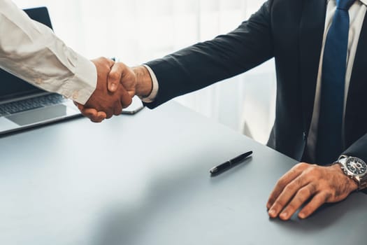 Business partnership meeting with successful trade agreement with handshake or greeting in corporate office desk. Businessman in black suit shaking hand after finalized business deal. Fervent