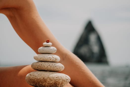 Woman bilds stones pyramid on the seashore on a sunny day on the blue sea background. Happy holidays. Pebble beach, calm sea, travel destination. Concept of happy vacation on the sea, meditation, spa