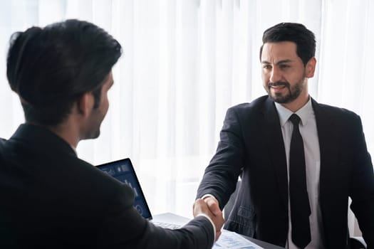 Closeup professional businessman shaking hands over desk in modern office after successfully analyzing pile of dashboard data paper as teamwork and integrity handshake in workplace concept. fervent