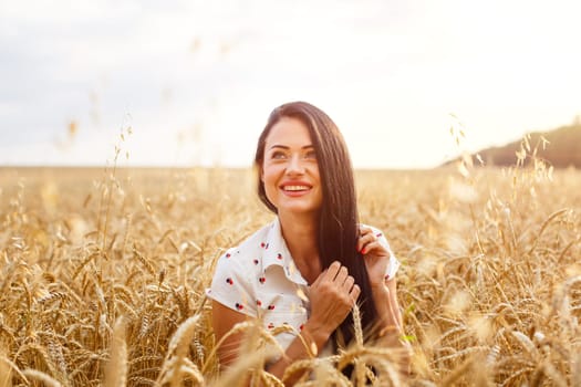 Beautiful young woman in wheat field. Cute brunette girl of Caucasian appearance in casual clothes is resting, happy in a ripe wheat field on a sunny day