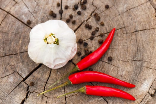 a head of garlic and red hot pepper on a cracked wooden stump background close-up on a sunny summer day. the row is sprinkled with black pepper peas