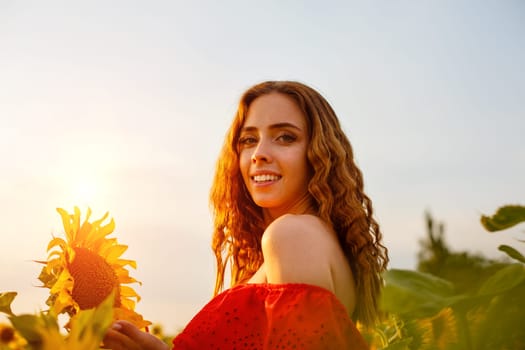 Beautiful curly young woman in sunflower field holding sunflower flower in hand . Portrait of young woman in sun smiling cute. Charming girl of Caucasian appearance with wavy hair in a red dress