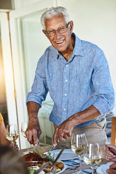 Dont mess with the master carver. a mature man carving a roast while enjoying lunch with his family outside