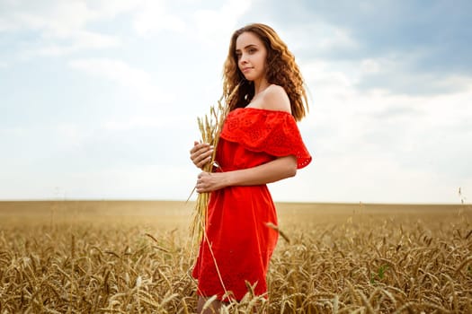 Young beautiful woman in golden wheat field. Happy woman in red dress enjoying life in field. Nature beauty. Outdoor lifestyle. Freedom concept. Summer field. Young beautiful woman golden wheat field