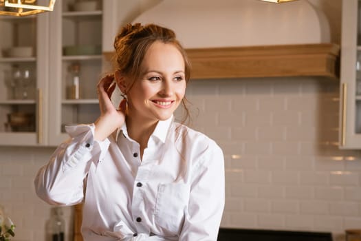 portrait of a young happy woman in a white shirt in the kitchen looking to the side