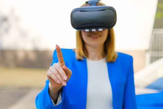 Business woman controls the virtual interface by pressing buttons with her finger in VR goggles in the park