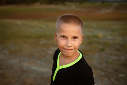 Happy little boy smiling. Guy of caucasian ethnicity in a black t-shirt looking at the camera on nature in summer