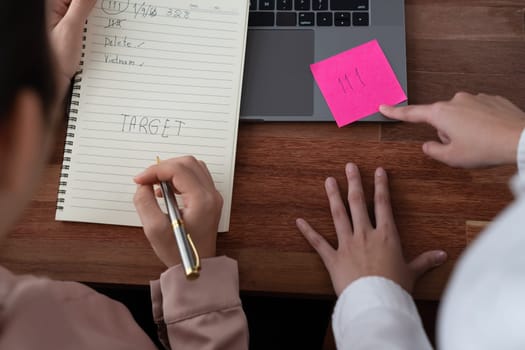 Two office lady colleague collaborating in modern office workspace, engaging in discussion and working together on laptop, writing post note as professional and modern office worker. Enthusiastic