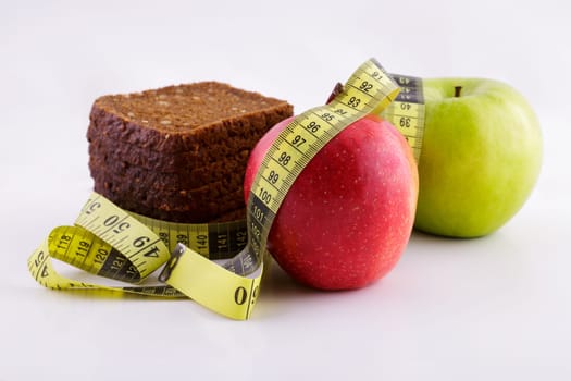 Black sliced bread and green and red apples lie on a white background with a yellow measuring tape, diet concept