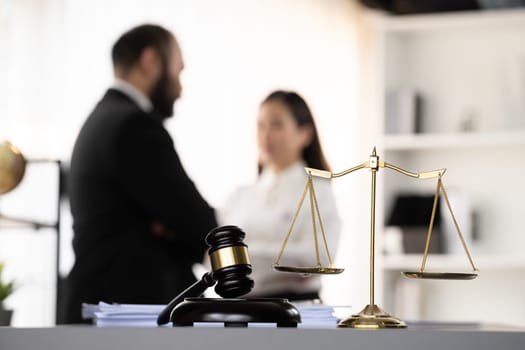 Balanced scale of justice and gavel hammer in focus on blurred background of lawyer colleagues discuss and plan for lawsuit in law firm office, as legal representatives. Equilibrium