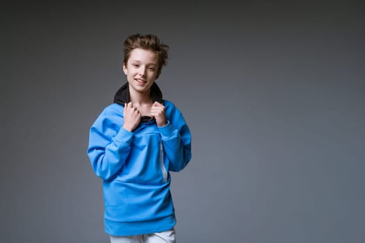 Portrait of a cute guy of European appearance with a snow-white toothy smile in a blue sweatshirt posing on a gray background