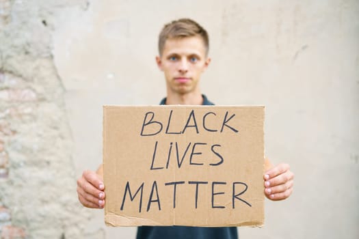 Man holding cardboard with the inscription, black life has value. Caucasian guy with a poster demonstrates his protest, against the background of a cement wall