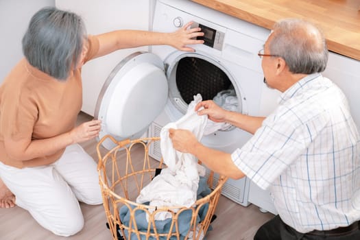 Senior couple working together to complete their household chores at the washing machine in a happy and contented manner. Husband and wife doing the usual tasks in the house.