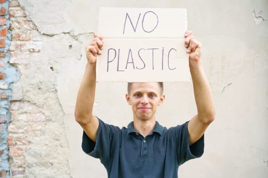 Caucasian guy holding the inscription no plastic. Environmental protection concept from garbage pollution . Young man protesting with placard banning plastic against cement wall background