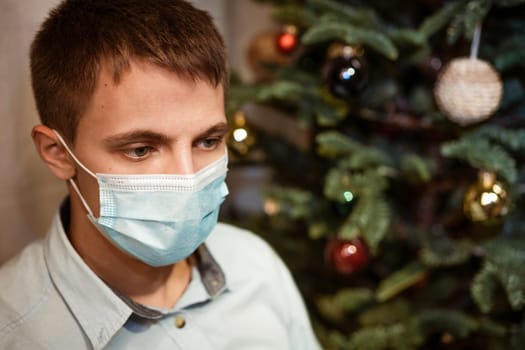 male portrait of Caucasian appearance close-up, in a protective mask against the background of a Christmas tree