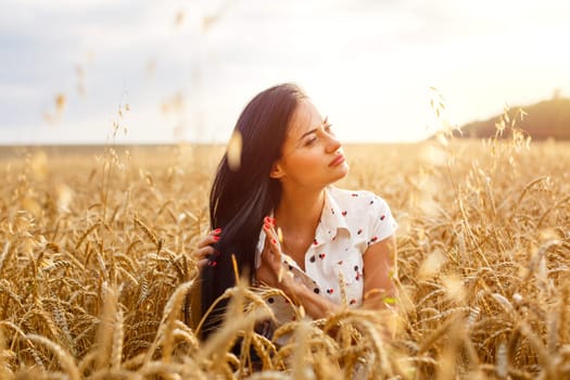 Beauty Girl Outdoors enjoying nature on wheat field. Beautiful Model girl with long hair on golden Field, Sun Light. Glow Sun. Free Happy Woman.