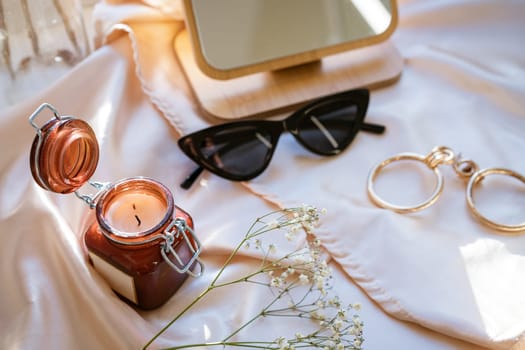 there is a decorative candle in a jar on the fabric, black glasses and jewelry with a mirror, soft focus