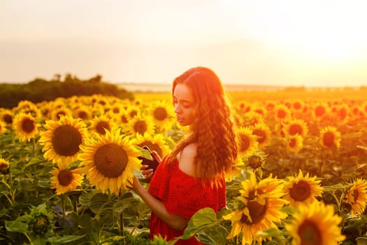 Female portrait of young woman in field of blooming sunflowers in rays of sunset . Cute girl of Caucasian appearance in evening, free and happy in red dress, stands in a field of bright sunflowers
