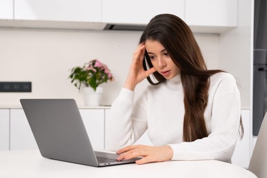 A stressed young woman thinks intensively while working at a computer at home.