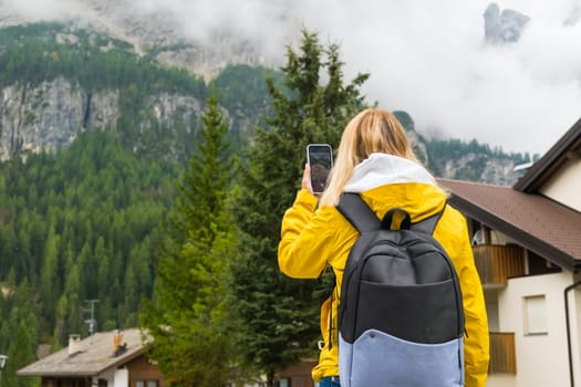 Tourist uses mobile phone for taking photos of moments of misty Alpine mountains. Woman makes photos of mountain hills covered with clouds