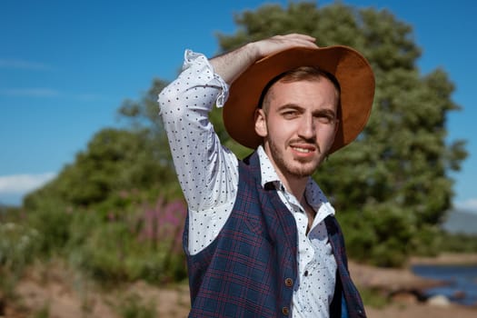 Young handsome man in a shirt and a hat on nature looks to the side during the day in summer