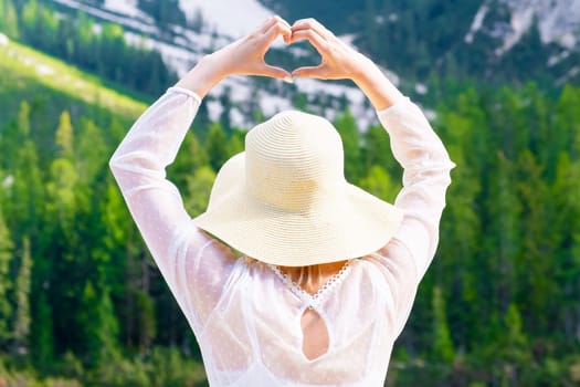 Blonde hair woman shows the heart with her hands on the background of the Dolomites and Lake Braies.