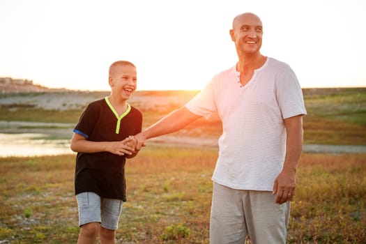 Son and dad standing against the backdrop of a colorful sunset. The relationship between father and son. Family's soulful walk in nature in the rays of the setting sun