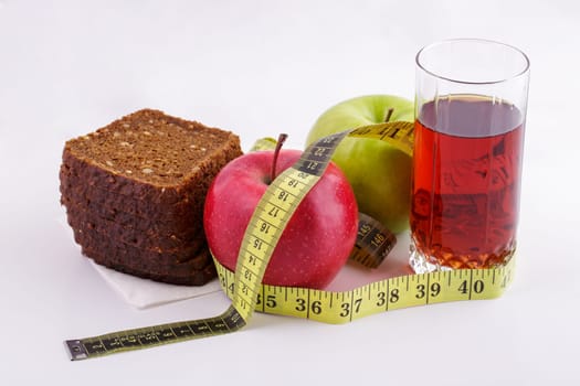 Rye bread with green and red apples and juice in a glass on a white plate with a yellow measuring tape. Diet and healthy food concept