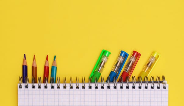 Colorful stationery is placed under a notebook on a yellow background, top view, for advertising.