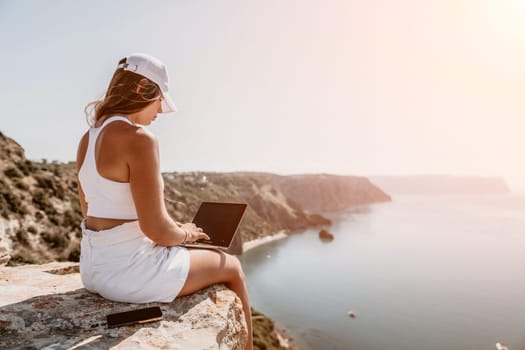 Digital nomad, Business woman working on laptop by the sea. Pretty lady typing on computer by the sea at sunset, makes a business transaction online from a distance. Freelance remote work on vacation