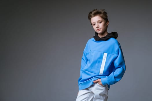 Portrait of a cute guy of European appearance smile in a blue sweatshirt posing on a gray background