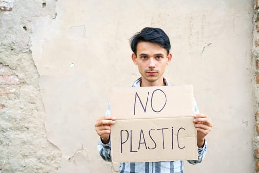 Young man with the inscription on the cardboard no plastic. Caucasian guy at a demonstration against environmental pollution, to help protect the environment. For a clean eco system on the planet