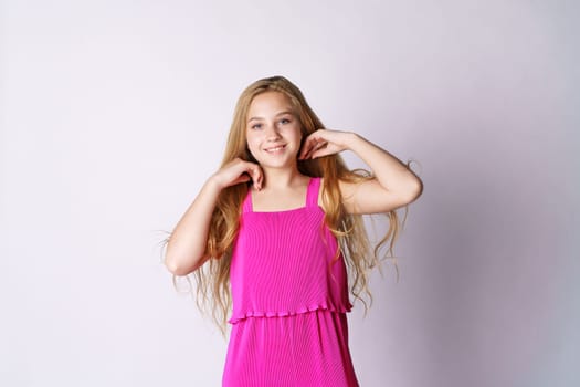 A cute and happy girl of Caucasian appearance in pink clothes on a white background plays with her long hair.