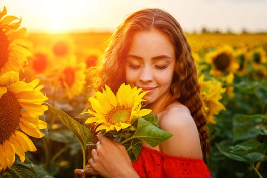 Beautiful curly young woman in sunflower field holding sunflower flower in hand . Portrait of young woman in sun smiling cute. Charming girl of Caucasian appearance with wavy hair in a red dress